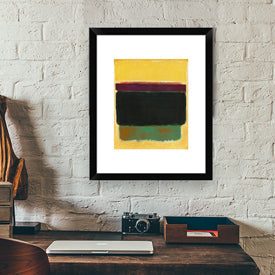 Framed abstract artwork on a brick wall with a desk and camera in the foreground.